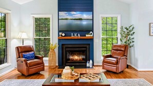 A living room with a fireplace, two leather chairs, a coffee table, and a view of a lake through the windows.