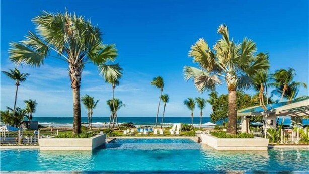 Una piscina con agua cristalina azul, rodeada de palmeras y vista al océano.