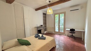 Une chambre avec un lit, un bureau, une cheminée et une vue sur la verdure environnante.