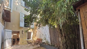 Une cour avec une table et des chaises, entourée de plantes de bambou et d’un petit jardin.