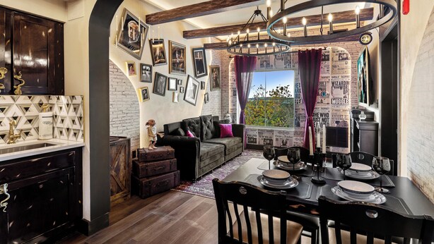 Un interior moderno con zona de comedor, cocina y sala de estar, que destaca por paredes de ladrillo visto, una araña y varias fotografías enmarcadas.