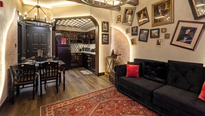 Un comedor con candelabro, un sofá negro con cojines rojos y una alfombra estampada.