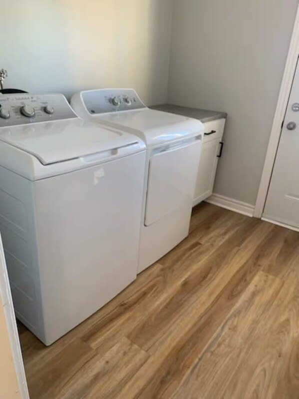A laundry room with two white front-loading washers and dryers, wooden flooring, and a white door.
