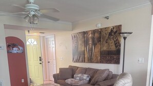Una sala de estar con un sofá de cuero marrón, un sillón blanco, una mesa de centro y una alfombra estampada.