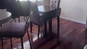 Un comedor con una mesa redonda y sillas, una lámpara colgante y un ventanal con persianas.
