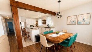 Uma sala de jantar com mesa e cadeiras de madeira, uma cozinha ao fundo e um corredor que dá para outro quarto.