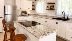 Cozinha com armários brancos, geladeira de aço inoxidável, torneira preta e bancada de granito.