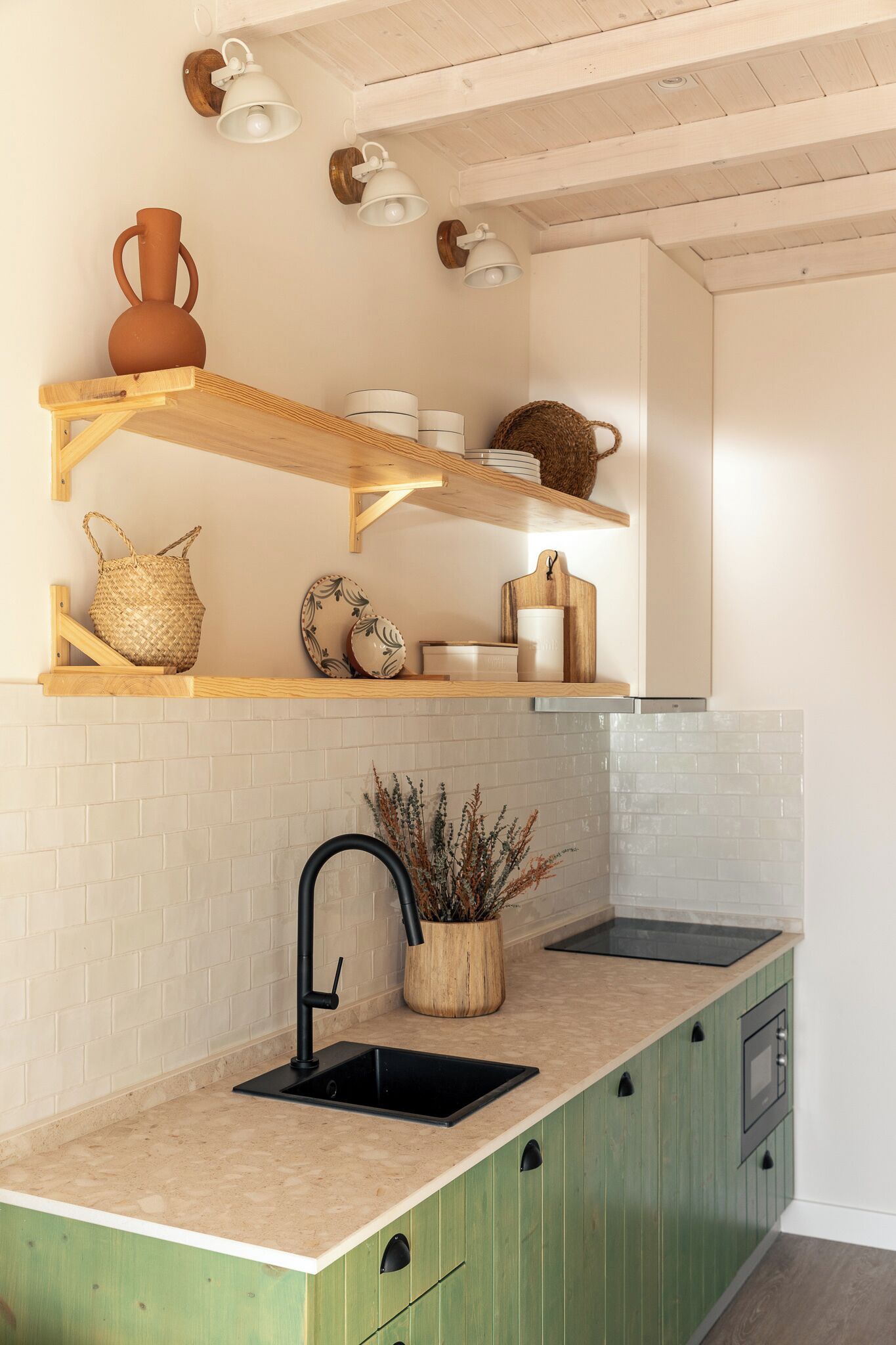 Cocina con armarios verdes, un lavamanos negro y repisas de madera con utensilios de cocina.