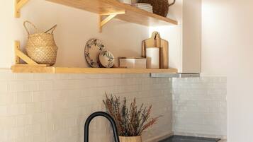 Cocina con armarios verdes, un lavamanos negro y repisas de madera con utensilios de cocina.