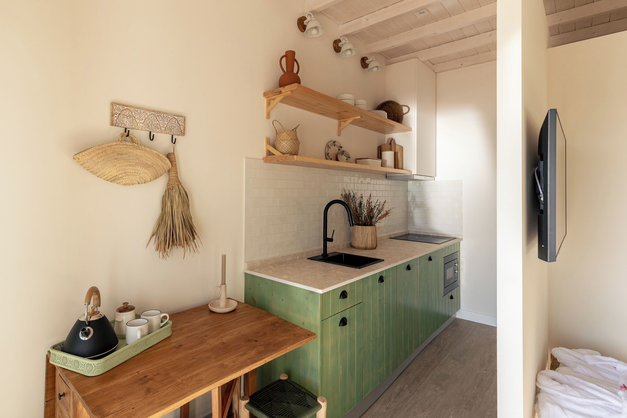 A compact kitchen with green cabinets, a wooden countertop, and a hanging basket.