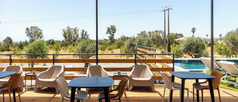An outdoor patio with tables and chairs, overlooking a pool and a natural landscape.