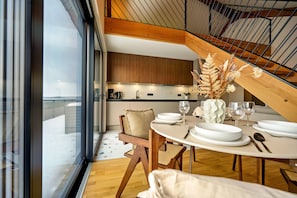 A modern dining area with a round table set for two, wooden chairs, and a view of the kitchen and balcony. - Suite #3 with lake view at Bärwalder See - SKAN-PARK (Klitten)