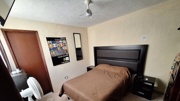 A hotel room with a bed, a nightstand, a desk with a chair, a standing fan, and a ceiling fan. - Independent room, 2 persons, near Peña de Bernal and vineyards. (Ezequiel Montes)