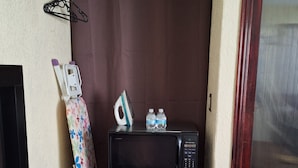 A compact room with a bed, a small table with a remote control, a microwave, and a water bottle. - Independent room, 2 persons, near Peña de Bernal and vineyards. (Ezequiel Montes)