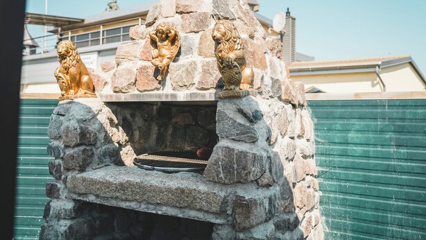 A stone barbecue grill with three golden statues on top. - Tiny house close to nature with barbecue area - pet-friendly & close to the lake (Lohmen)
