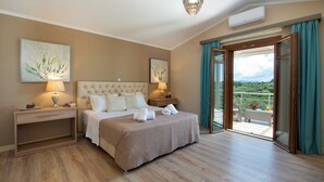 A bedroom with a large bed, two bedside tables, a nightstand, and a view of a balcony with outdoor furniture.