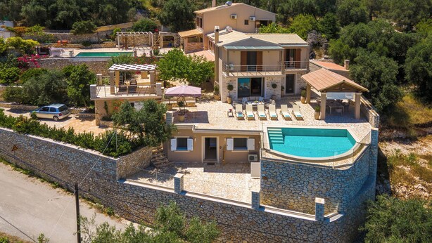 A multi-story villa with a swimming pool, outdoor seating, and a stone wall.
