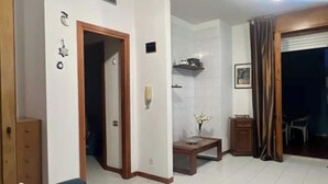 A living room with a sofa, a wooden cabinet, a small table with a vase, and a doorway leading to another room.