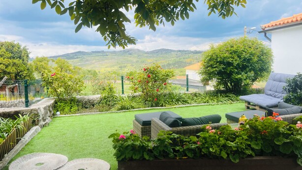 Une terrasse avec des meubles d’extérieur, une pelouse verdoyante et une vue sur des collines en arrière-plan.