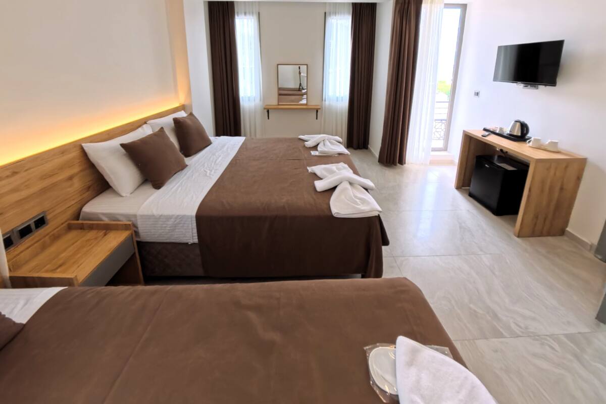 A hotel room with two beds, a TV, a desk with a kettle, and a mirror.