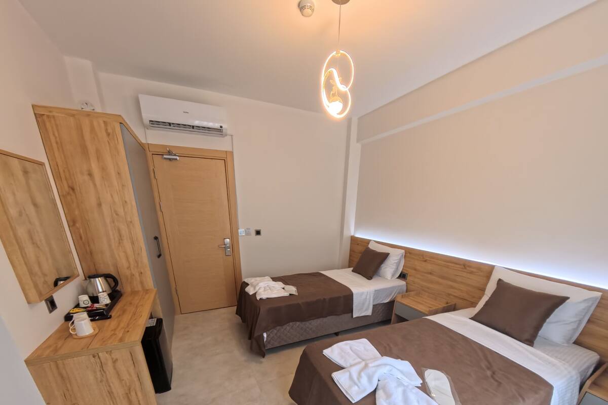 A hotel room with two beds, a wooden wardrobe, a coffee station, and an air conditioning unit.