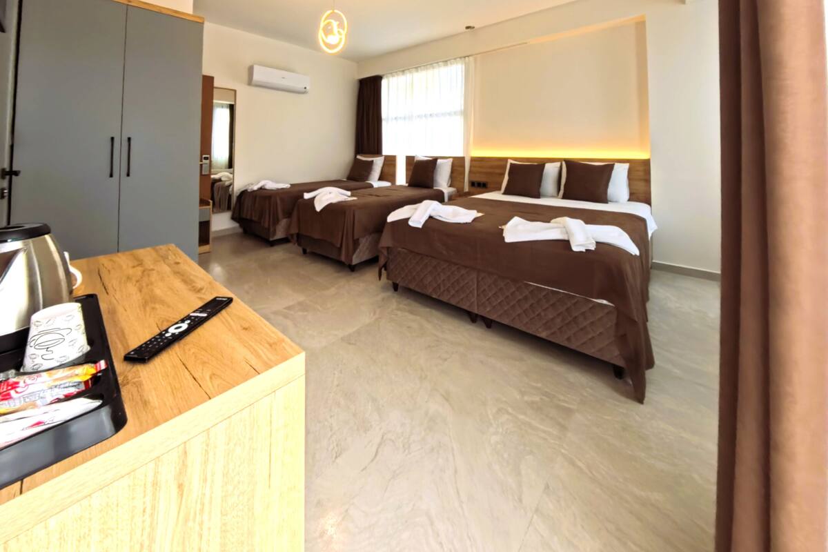 A hotel room with two beds, a wooden desk with a kettle, a remote control, and a minibar.