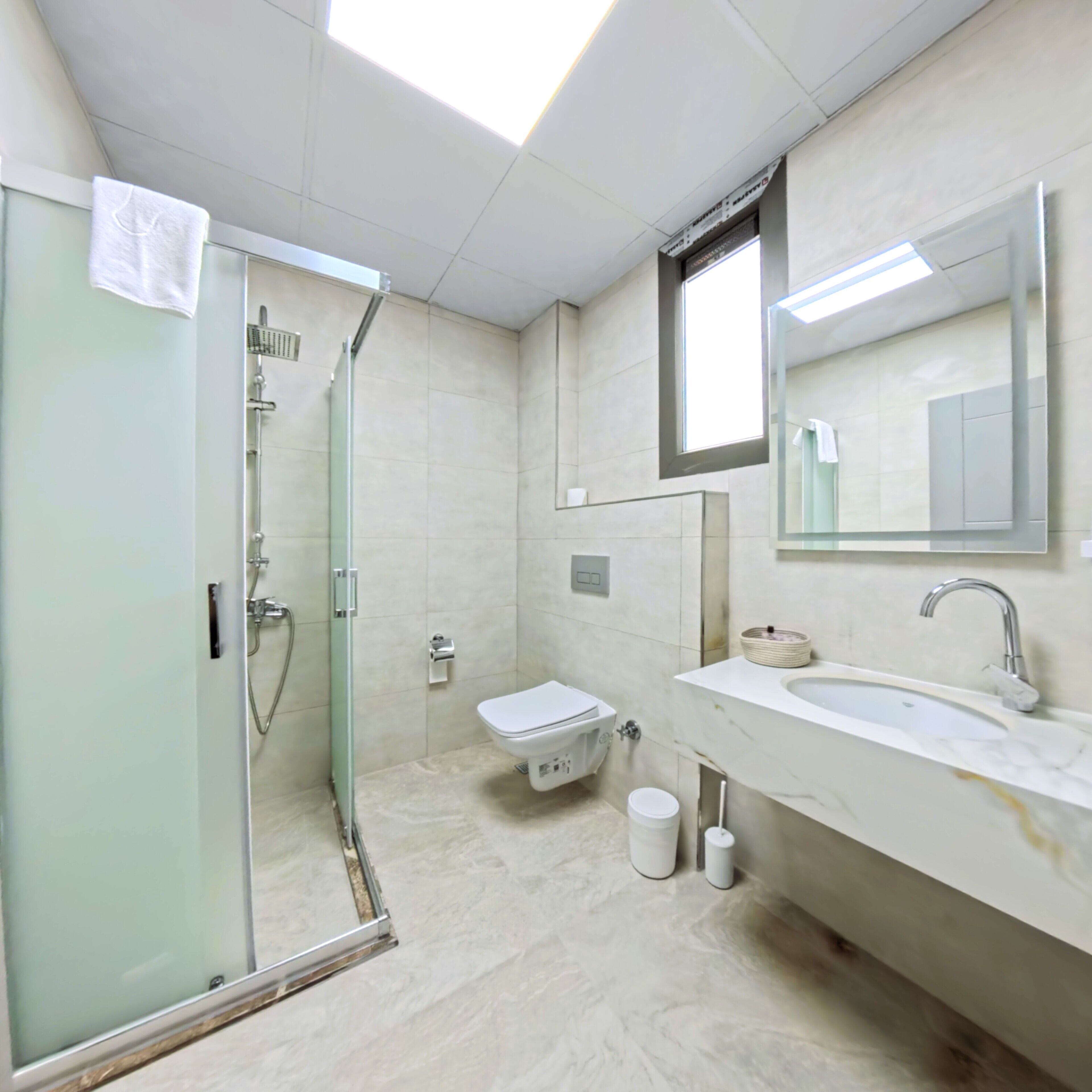 Une salle de bain moderne avec une douche à parois de verre, des toilettes et un lavabo surmonté d’un miroir.
