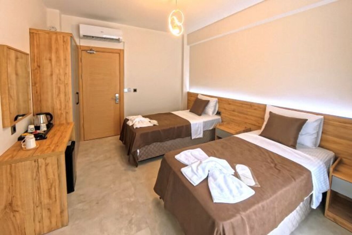 Habitación de hotel con dos camas, un armario de madera, un escritorio con hervidor y un equipo de aire acondicionado.