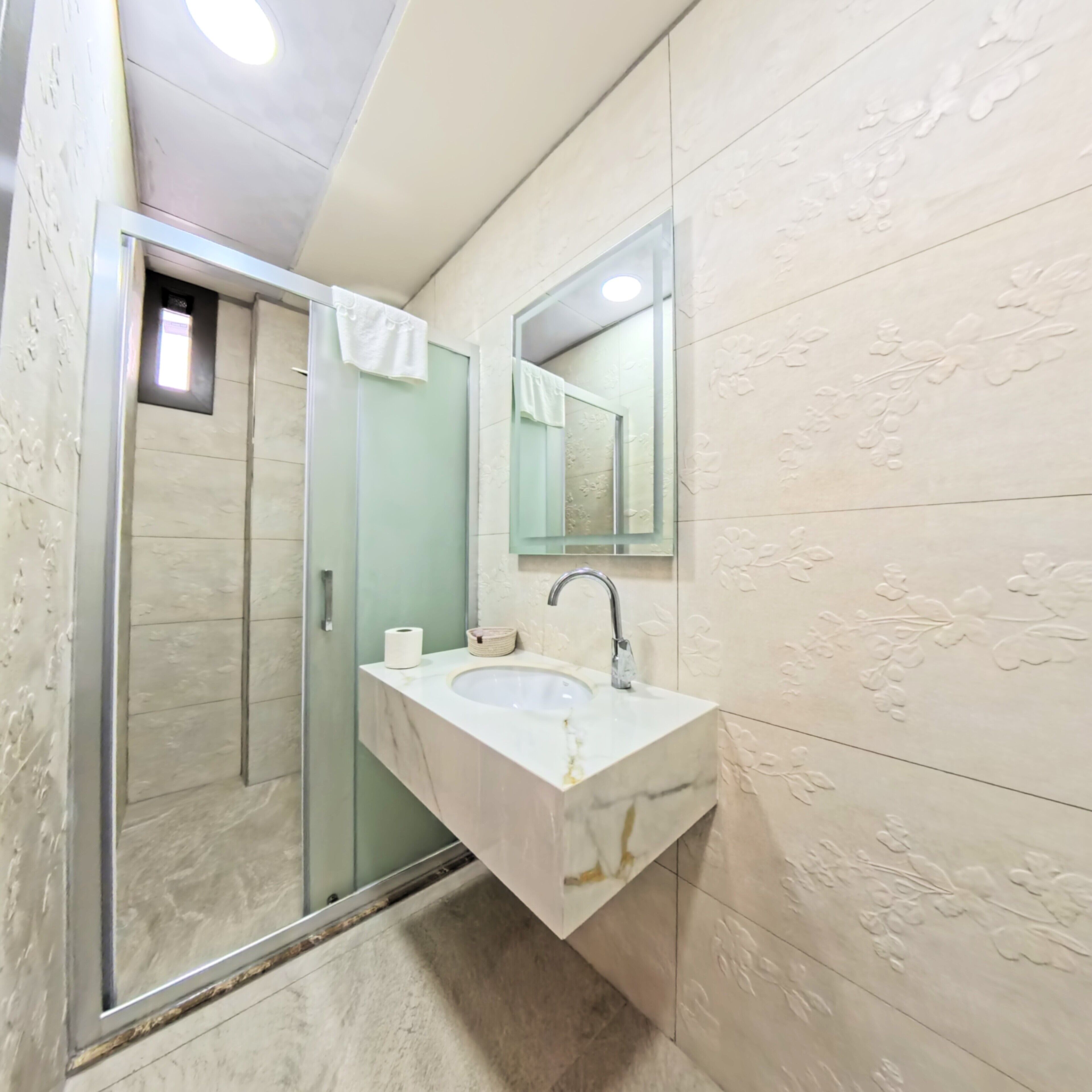 Un baño con cabina de ducha de vidrio, un lavamanos con espejo y azulejos decorativos.