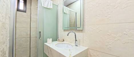 Un baño con cabina de ducha de vidrio, un lavamanos con espejo y azulejos decorativos.