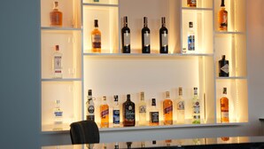 Un espace bar avec des étagères remplies de bouteilles d’alcool, des suspensions lumineuses et un comptoir.