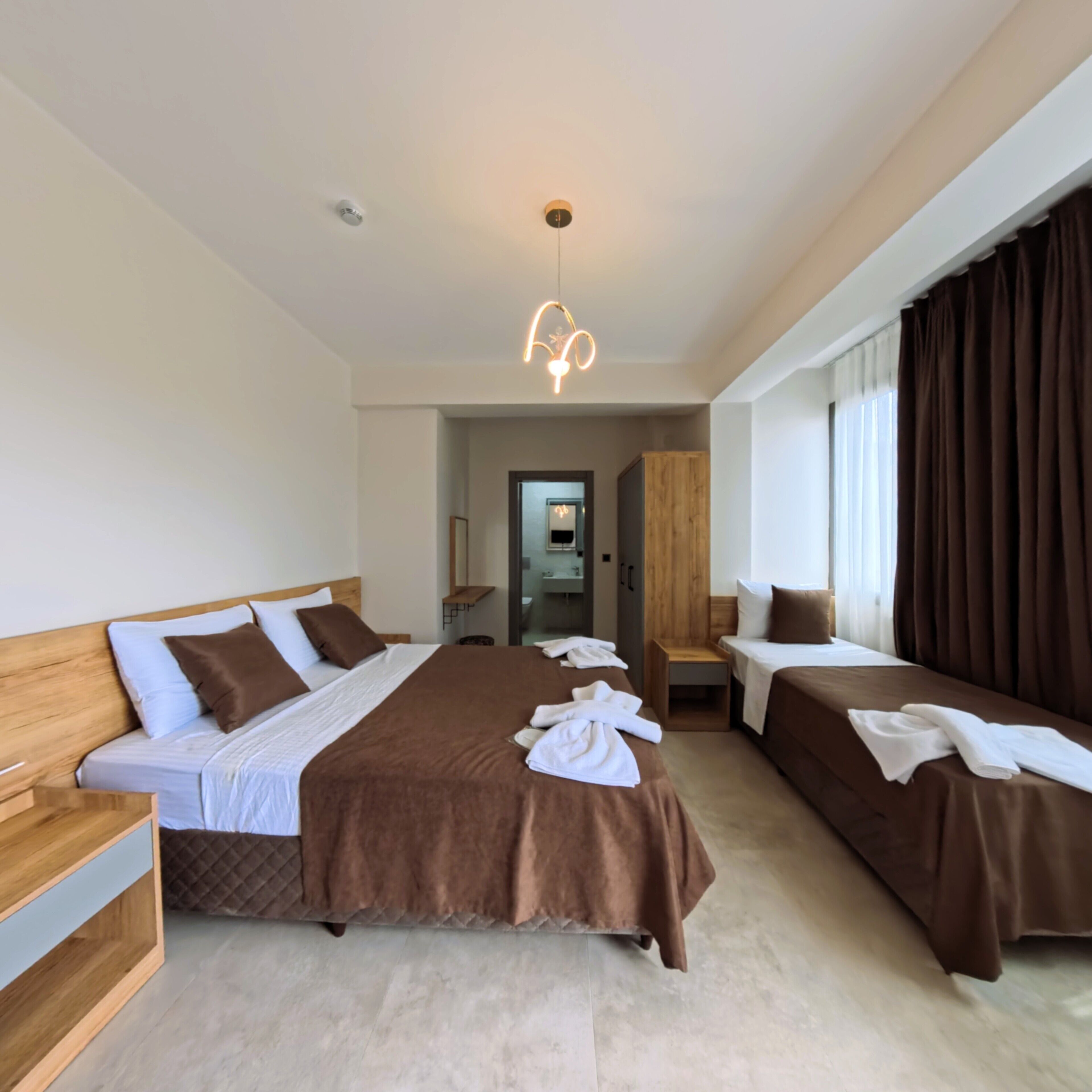 Una habitación de hotel moderna con dos camas, un cabecero de madera, un espejo grande y una lámpara en el techo.