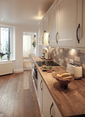 A modern kitchen with white cabinetry, a wooden countertop, and a view of the adjacent living area. - South Lanes Coastal Cottage with Patio (Brighton and Hove)
