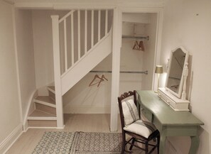 A room with a staircase, a vanity with a mirror, and a chair.