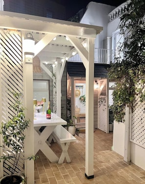An outdoor patio area with a white pergola, a table with a bottle and glasses, and potted plants. - South Lanes Coastal Cottage with Patio (Brighton and Hove)