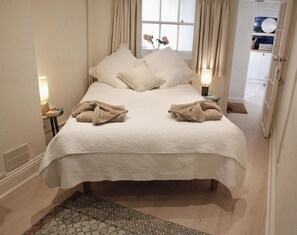 A neatly made bed with a white bedspread and two towels, a bedside lamp, and a window with curtains.