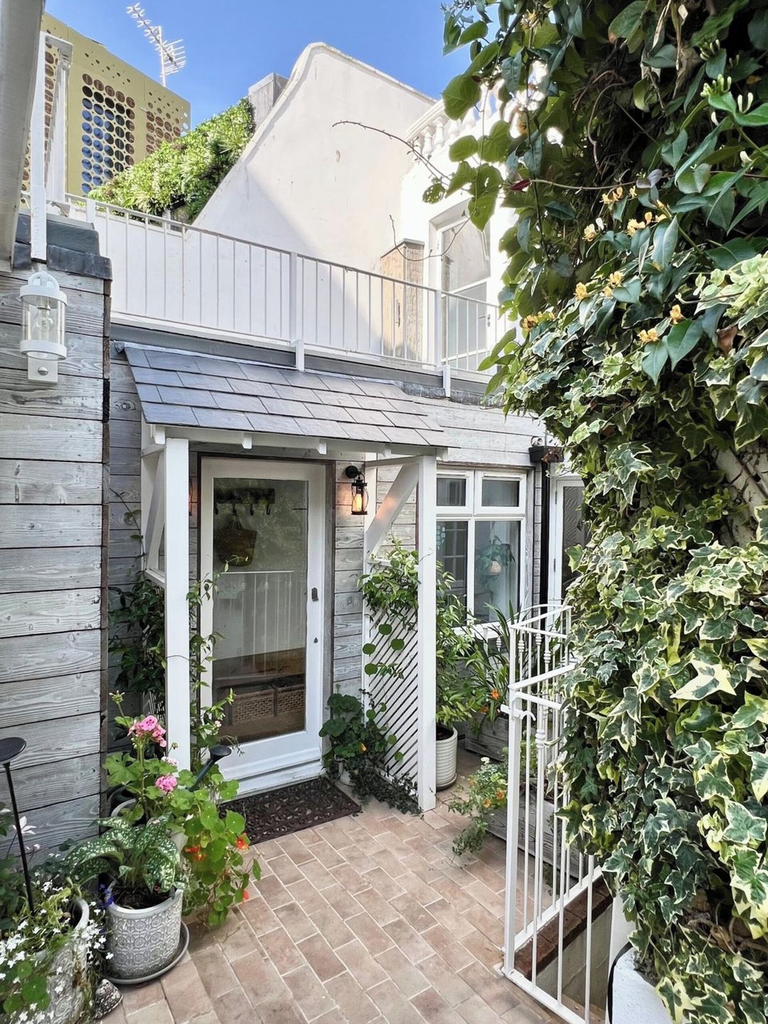 Ein Wohnhaus mit überdachter Veranda, einem Ziegelweg und Kübelpflanzen.