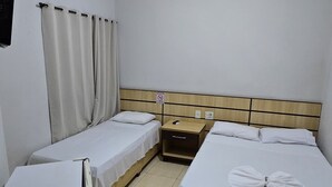 Habitación de hotel con dos camas individuales, una mesita de noche con teléfono, una mesita auxiliar, un aire acondicionado instalado en la pared y una lámpara en el techo.