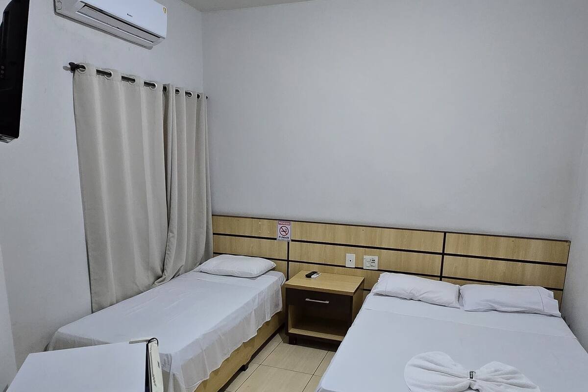 A hotel room with two single beds, a small bedside table with a phone, a nightstand, a wall-mounted air conditioner, and a ceiling light.