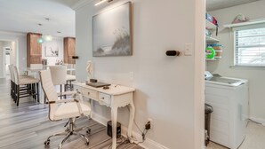 Una cucina moderna con mobili bianchi, un'area pranzo con tavolo e sedie bianche, e un angolo lavanderia con lavatrice.