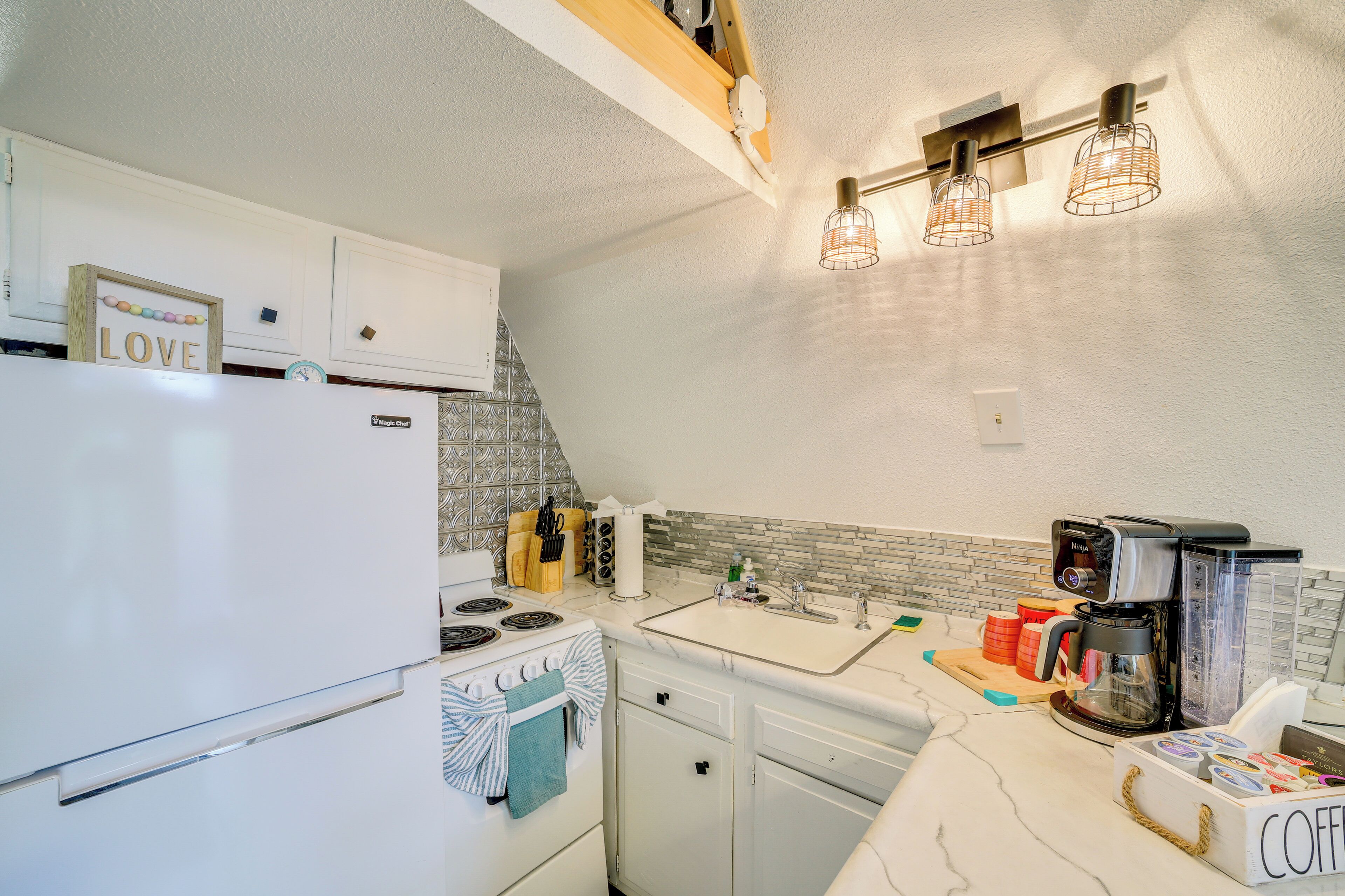 A modern kitchen with white cabinets, a stove, a sink, and a coffee maker.