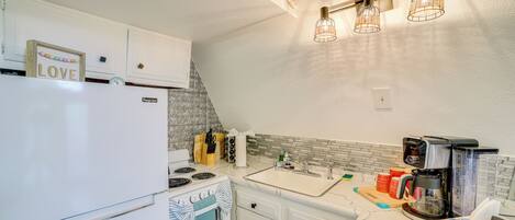 A modern kitchen with white cabinets, a stove, a sink, and a coffee maker.