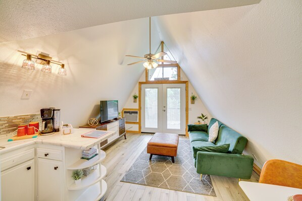 A cozy, well-lit room with a kitchenette, a green sofa, and a ceiling fan.