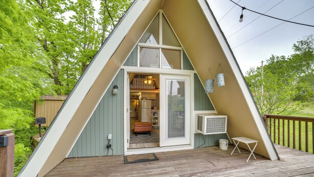 Eine dreieckige A-Form-Hütte mit einer Holzterrasse, einer Glastür und einer kleinen Sitzgelegenheit im Freien.