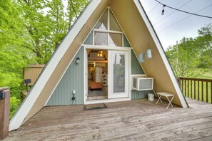 A triangular A-frame cabin with a wooden deck, a sliding glass door entrance, and a small outdoor seating area. - Cozy Cabin w/ Fire Pit: Walk to Lake Taneycomo! (Rockaway Beach)