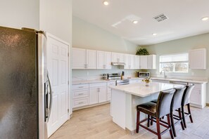 Une cuisine moderne avec des meubles blancs, des appareils en acier inoxydable et un îlot central doté de tabourets de bar.