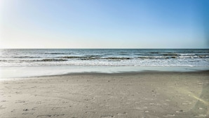 A beach with footprints in the sand and waves approaching the shore.