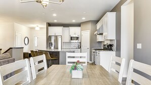 Una cucina moderna con mobili bianchi, un'isola centrale e un'area pranzo con tavolo e sedie in legno.