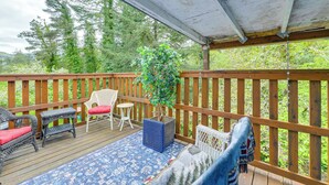 Une terrasse extérieure couverte, dotée de rampes en bois, de meubles en osier et d’une plante en pot.