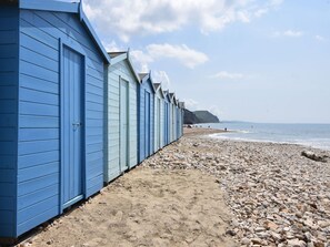 A row of beach huts with a pebble beach and ocean in the background. - Damson Tree Cottage (Bridport)